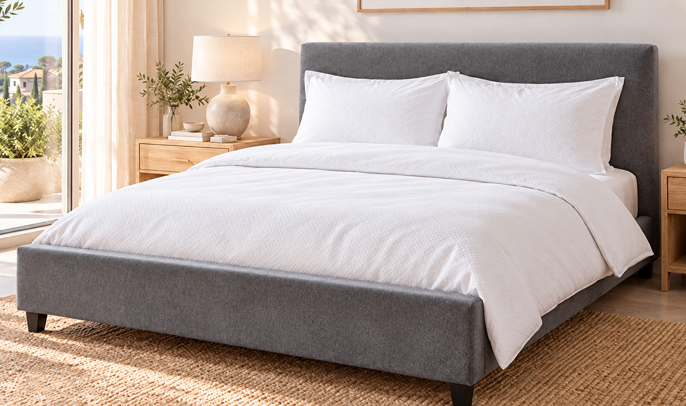 Gray upholstered bed with white bedding in a sunlit bedroom